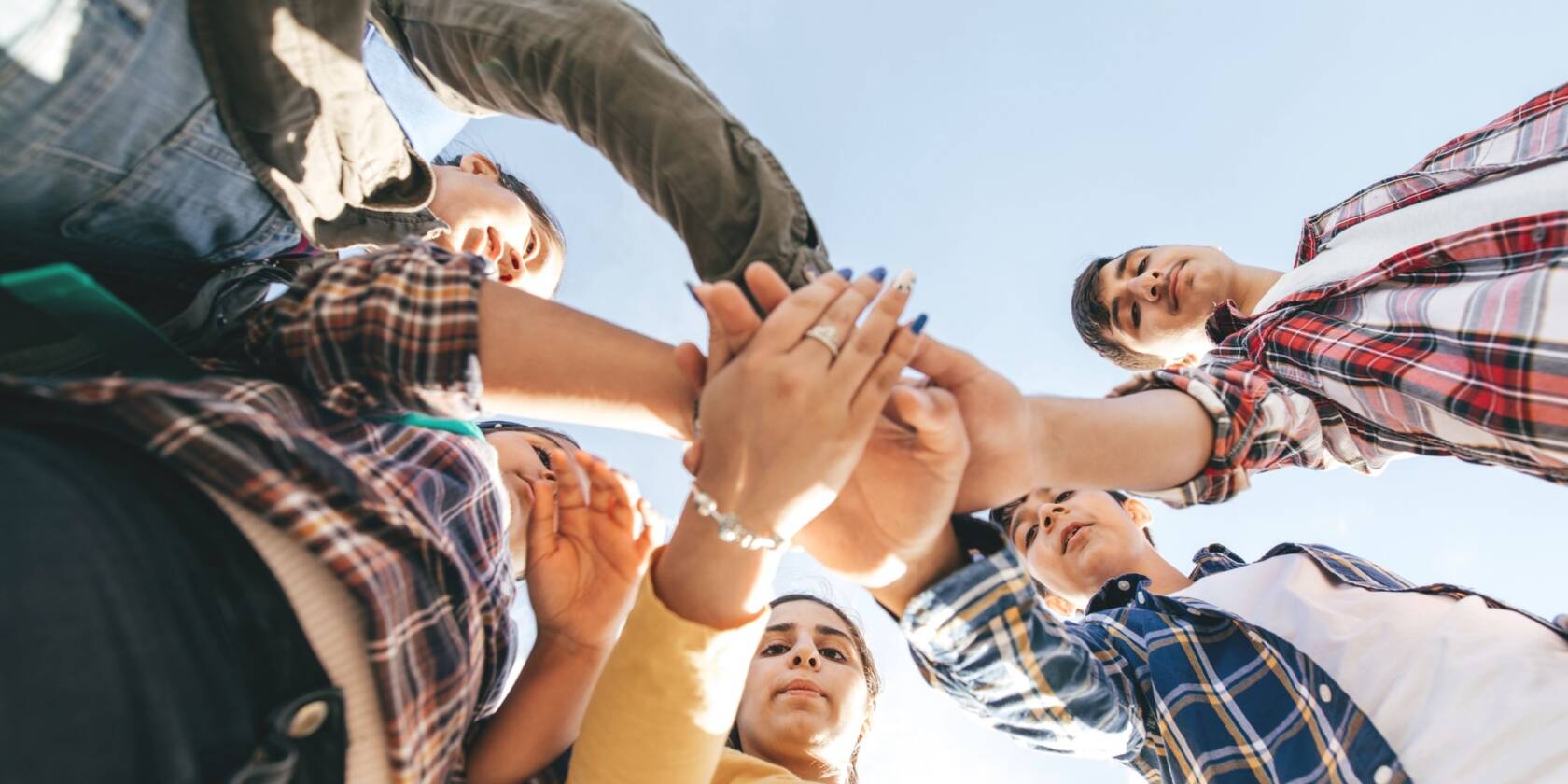 Several people are standing in a circle and they hold their hands in towards the centre.