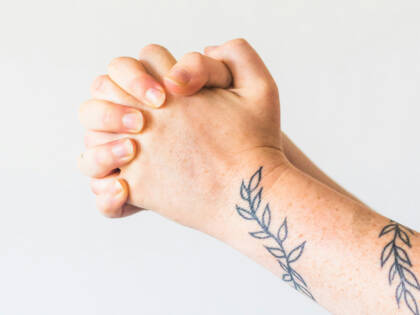 Hands held together in prayer. There is a tattoo of blue leaves on the arm.