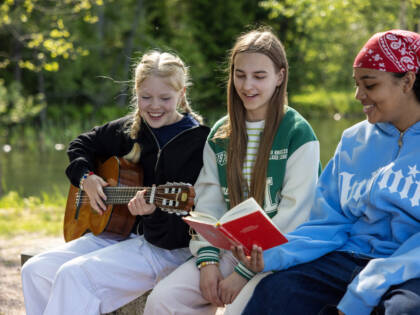 Three girls are singing. One has a guitar and another a song book.
