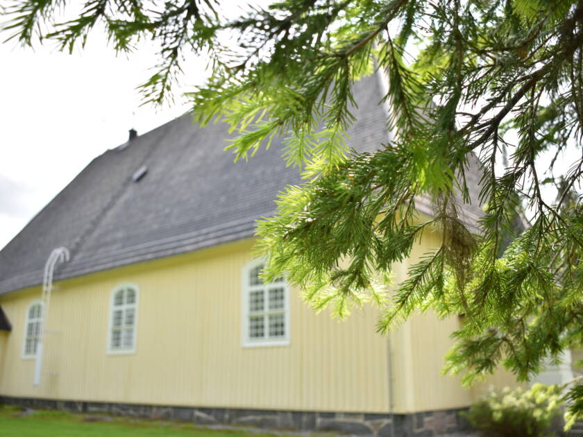 Aurejärven kirkon seinää kuvattuna havupuun oksiston takaa.