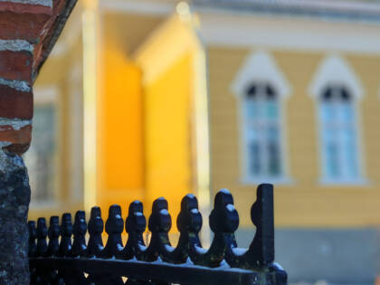 Ylöjärven kirkkomaan portin koristeellinen yläreuna lähikuvassa. Taustalla siintää utuisena kirkon keltapintaista hahmoa.