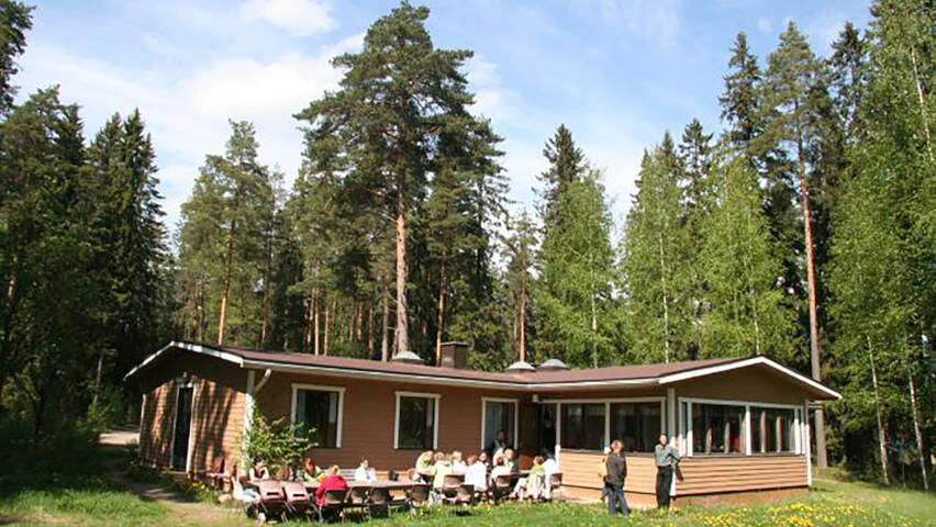 Lammasniemen leirikeskuksen rakennus kuvattuna kesällä. Rakennuksen edustalla on ihmisiä.
