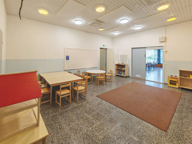 Vuorentaustan seurakuntatalon huone, jossa on seinän vieressä lasten pöytiä ja tuoleja. Kuvassa näkyy myös pätkä tyhjää nukketaloa sekä pieni leluhylly.