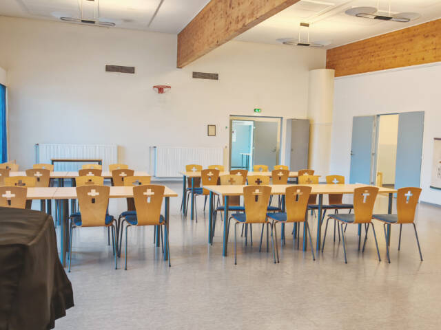 Vuorentaustan seurakuntatalon salissa pitkiä pöytiä ja niiden ääressä tuoleja. Tilan kulmasta avautuu vierekkäisiltä seinämiltä ovet eri suuntiin.